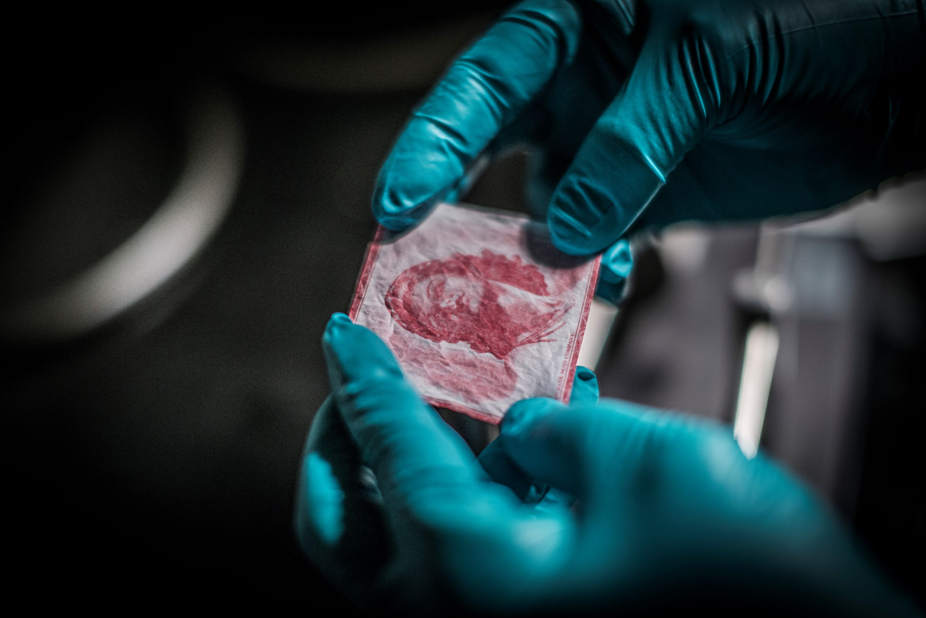 GLoved hands inspecting a piece of banknote paper